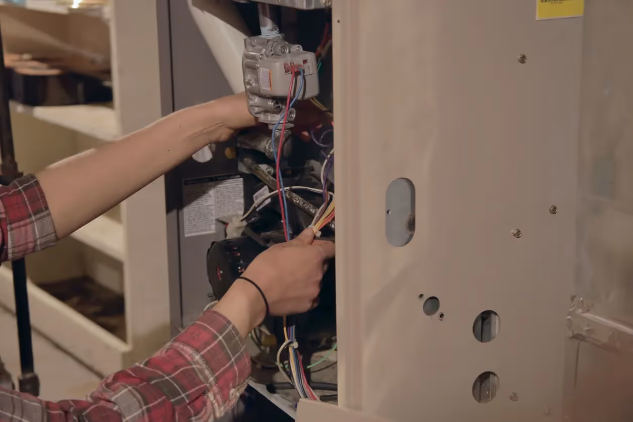 A close-up of hands working on the intricate wiring and components inside a furnace or HVAC unit.