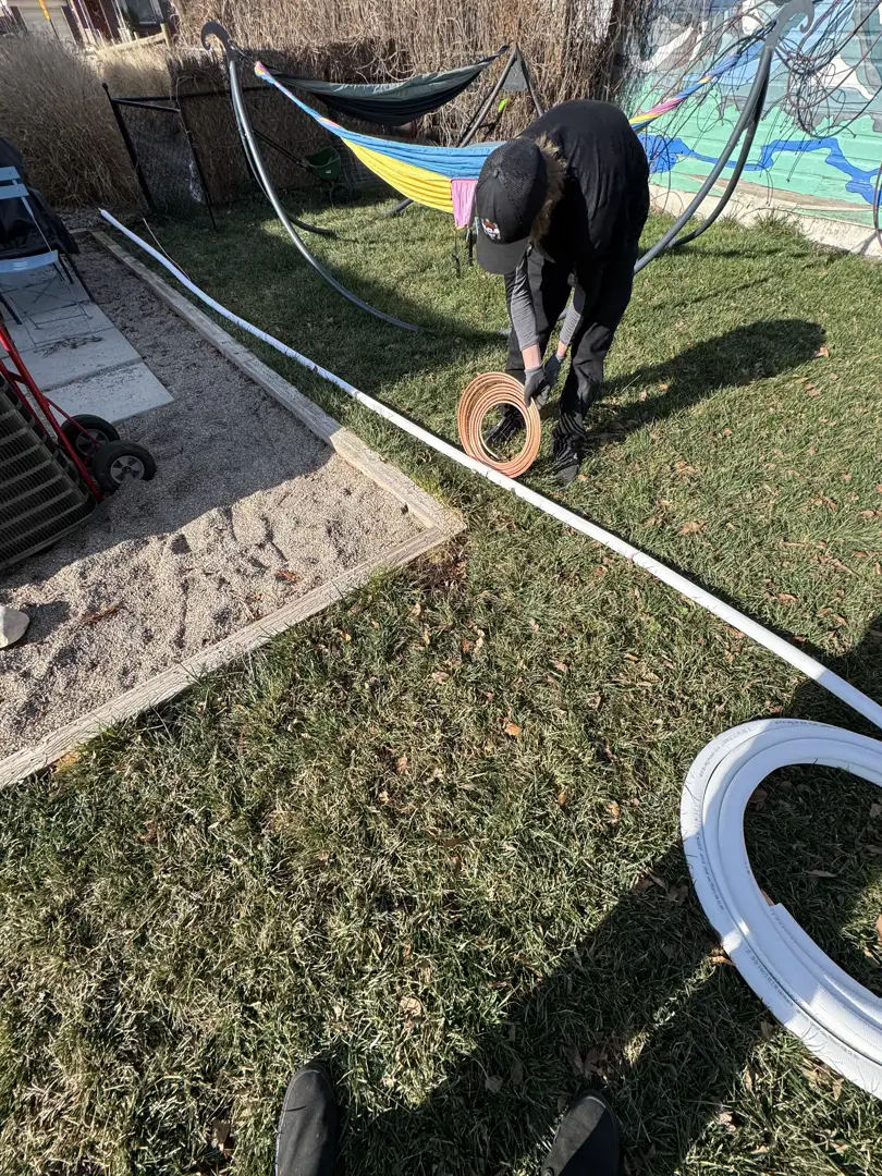 A technician inspecting copper refrigerant lines connecting the indoor and outdoor units of a home HVAC system