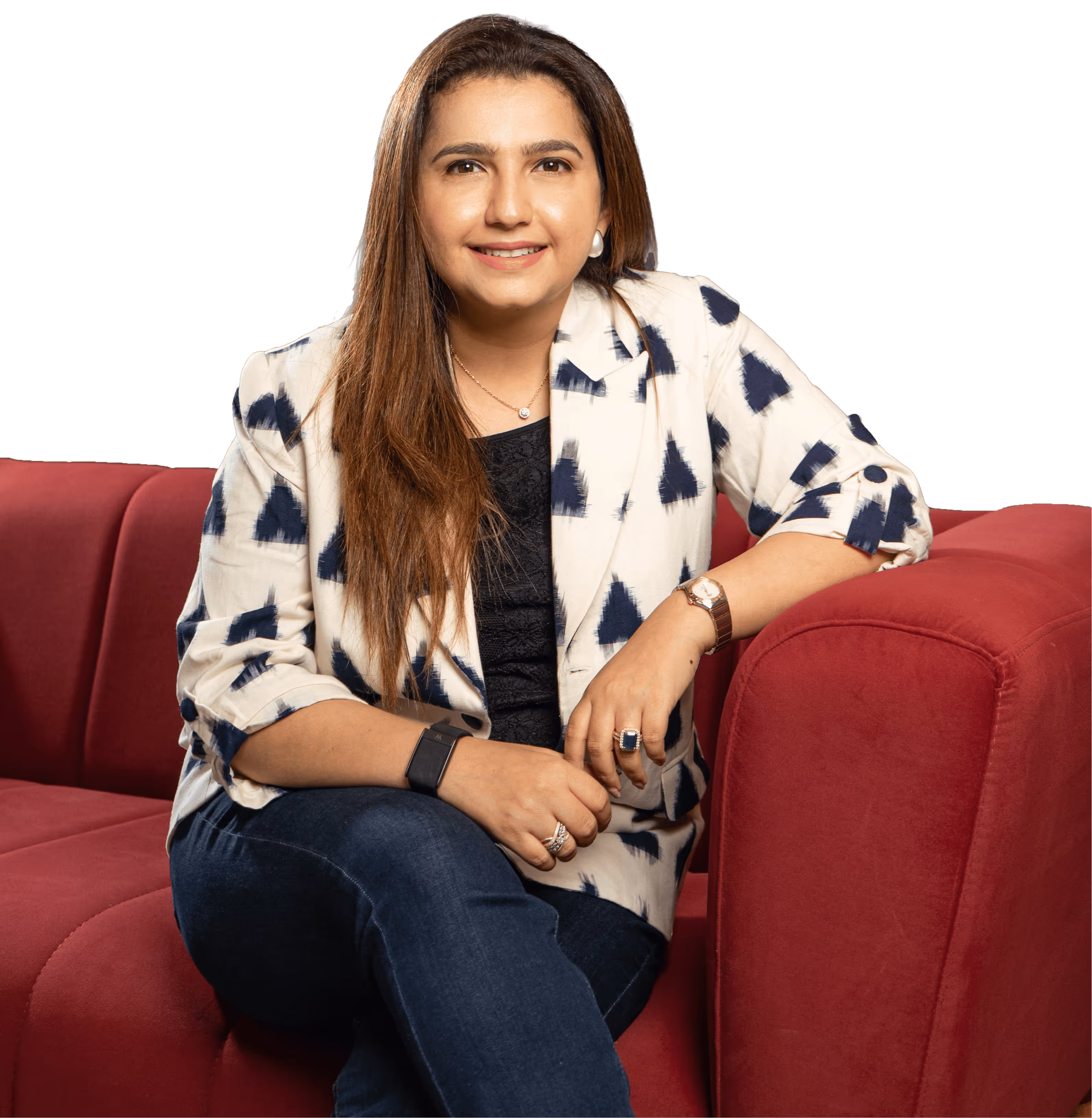 Woman with long hair in patterned blazer and jeans sitting on a red sofa, smiling at the camera.