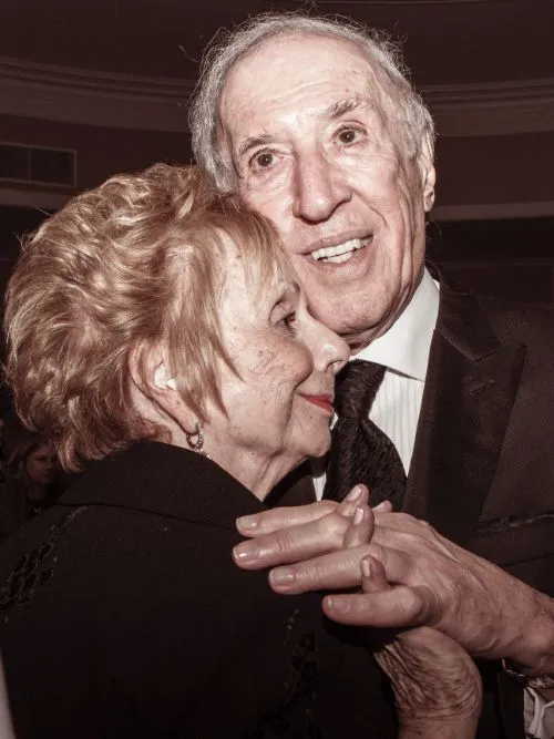 A mature couple standing together in an embrace on their wedding anniversary