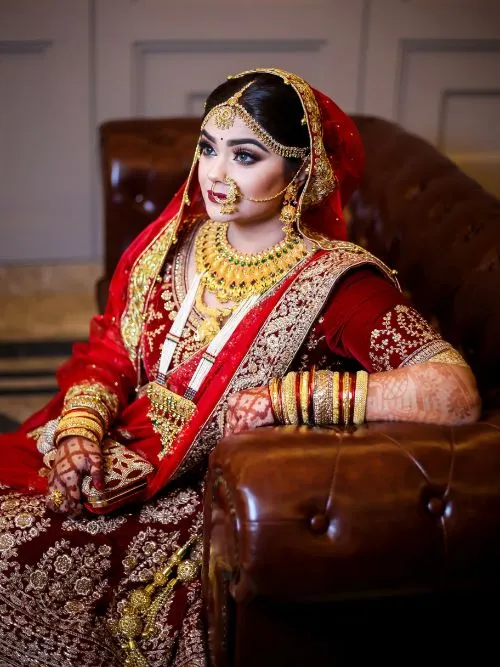 Beautiful Asian bride wearing a red and gold dress with ornate jewellery posing for a photo