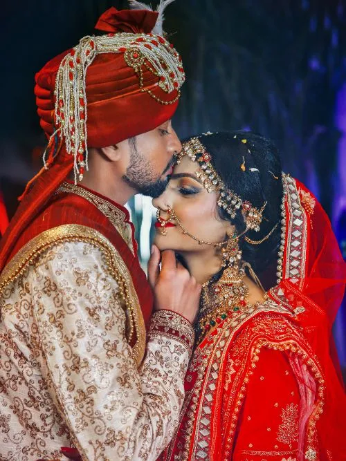 Asian couple in traditional wedding costumes stood facing each other before a camera