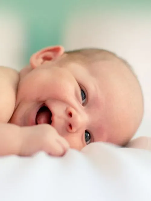 Portrait photograph of a young baby boy lying on a white blanket with his thumb in his mouth