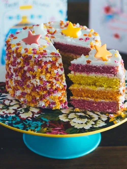 A multi-layered birthday cake decorated with stars being cut just after singing happy birthday