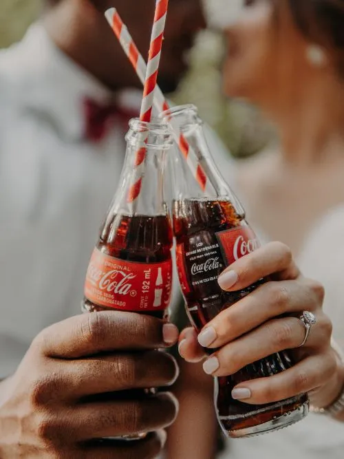 A photograph of two people holding branded Coca-Cola bottles up to the camera