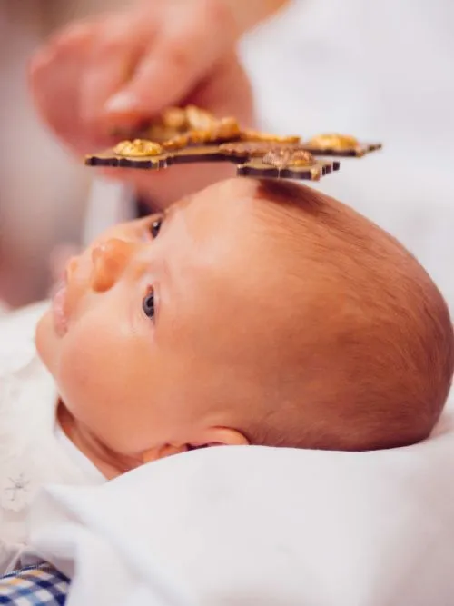 Baby being photographed as it Christened in a church near a font with a gold cross