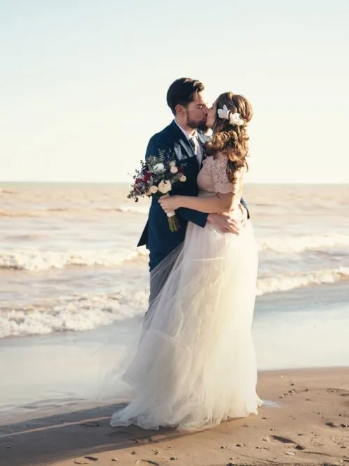 A well-dressed couple standing on a beach kissing in a cinematic wedding video shoot