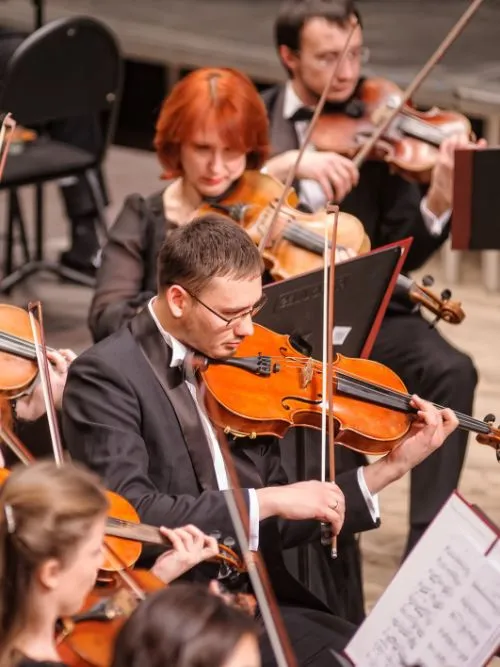 Several violinists performing in a classical concert being filmed in a large music hall