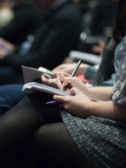 Delegates being filmed as they sit taking notes at a business conference