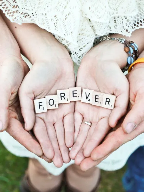 Photograph of a newly engaged couple holding hands with a sign saying 'forever'