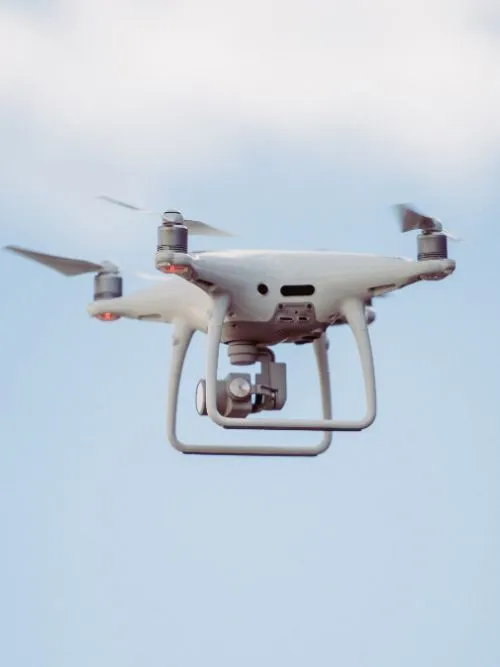 A white DJI Phantom drone hovering in the air and filming