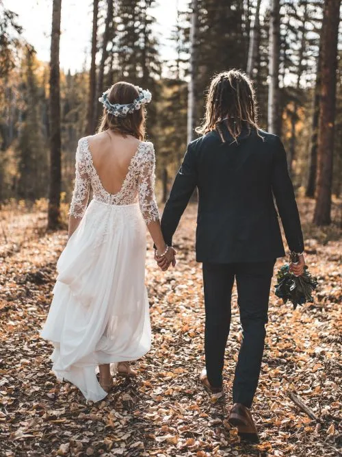 A man and woman who have eloped holding hands as they walk through a forest