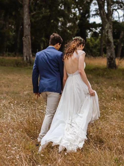 Photograph of a young man and woman walking through a field for an elopement wedding shoot