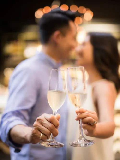 A happy couple holding champagne and kissing after they have got engaged