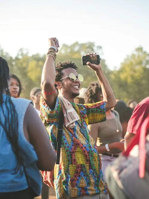 Photograph of a jubilant young man wearing glasses at a festival dancing and enjoying himself
