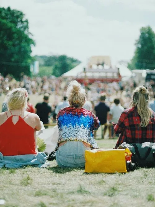 A view of a festival stage shot over the shoulder of three people sat on the ground