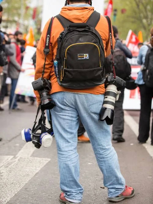 A freelance photographer holding two Canon 1DX cameras looking towards an event