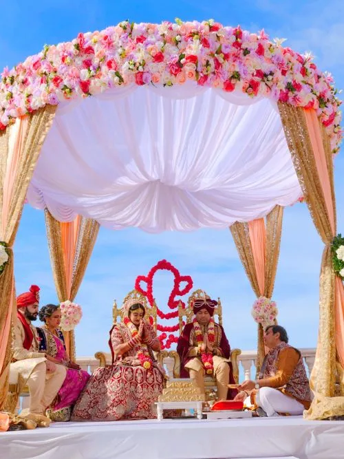 In Indian bride and groom sitting under a mandap whilst their Hindu wedding ceremony is filmed