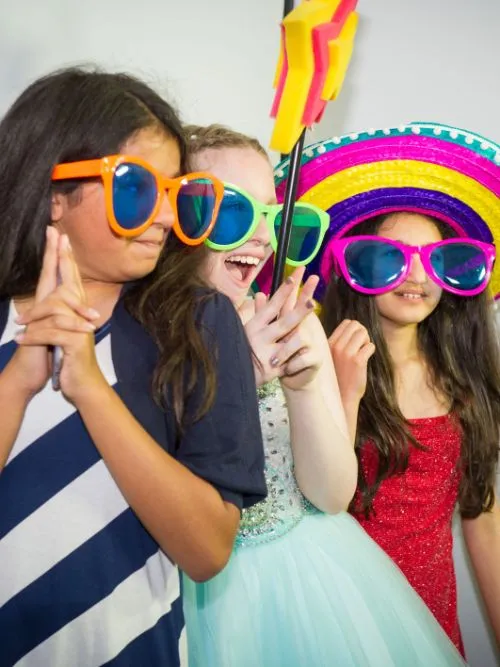 Three children wearing funny glasses and hats being filmed at a kid's party