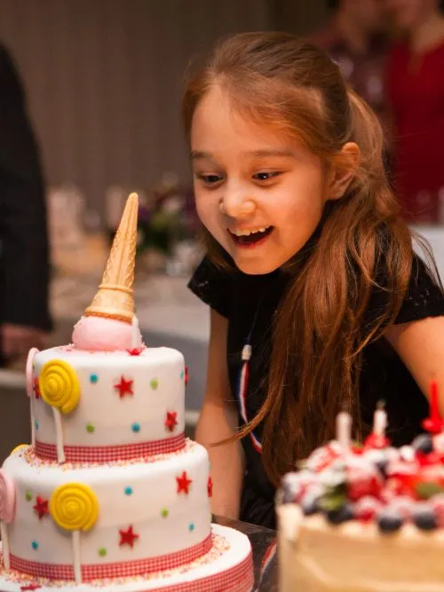 Photograph of a happy young girl blowing out candles on a cake at a kid's party