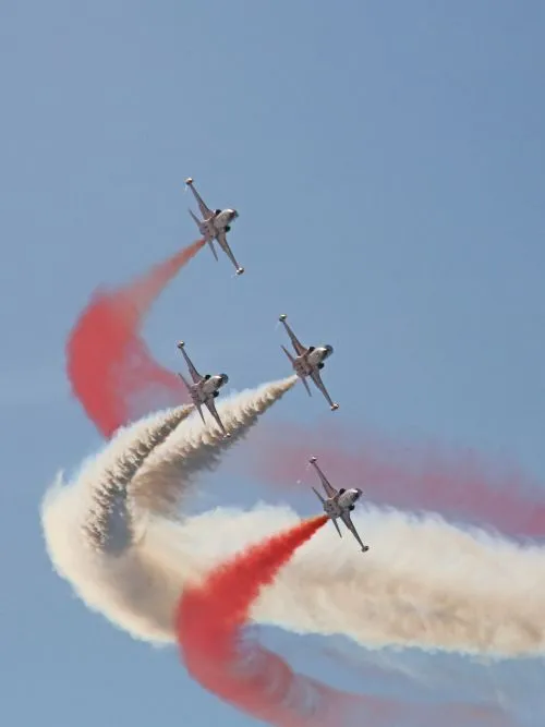 Long lens photo of a formation of planes with red and white smoke at a live airshow event