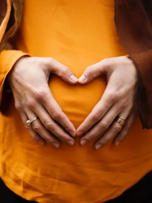 Portrait photo of a pregnant woman with her hands shaped like a heart in front of her baby bump