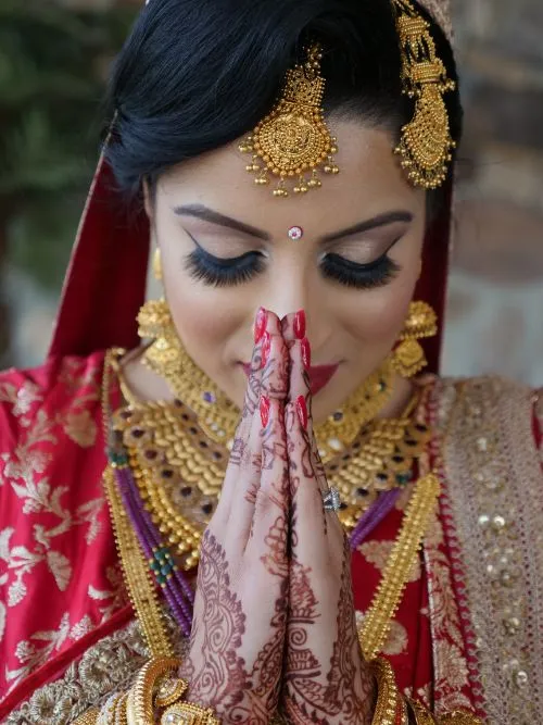 A Sikh bride wearing a red and gold dress praying before her Anand Karaj wedding ceremony
