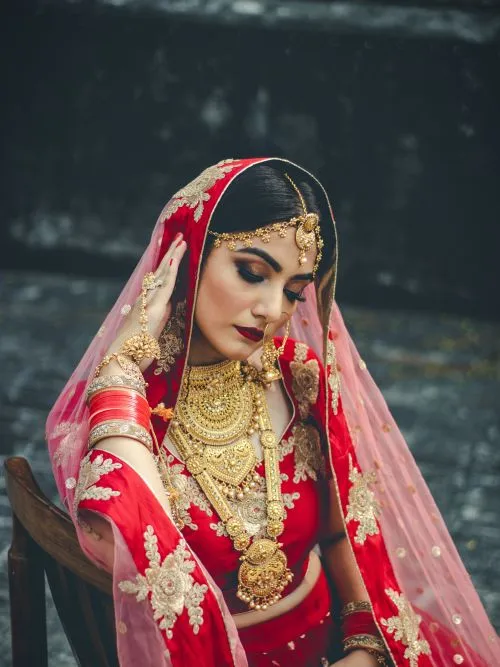 A Sikh bride sat in a chair posing for a photograph wearing a tradition Punjabi wedding dress