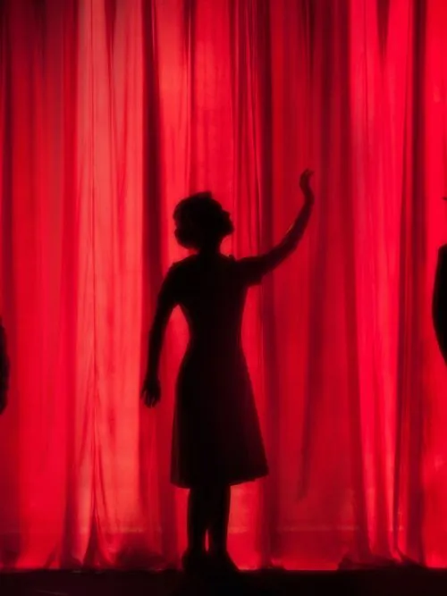 Silhouette image of an actress on stage with a red curtain in the background behind