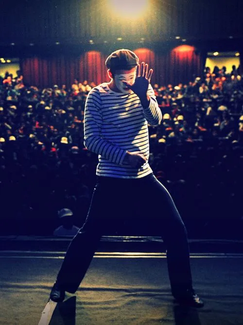 A mime artist on stage in a theatre show being filmed with the audience behind him