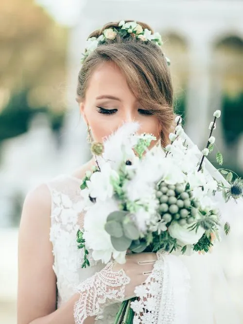 A bride in a white dress being filmed smelling her bouquet before the wedding ceremony
