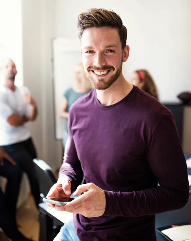 A young creative man dressed in a mauve jumper smiling into the camera
