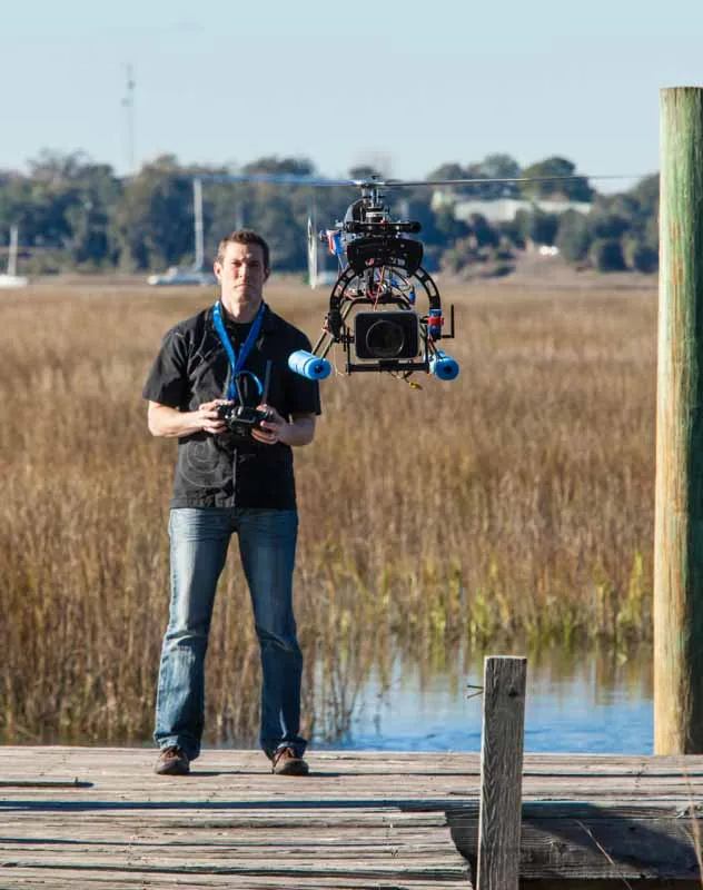 A mature man with a radio controller flying a heavy single rotor drone camera