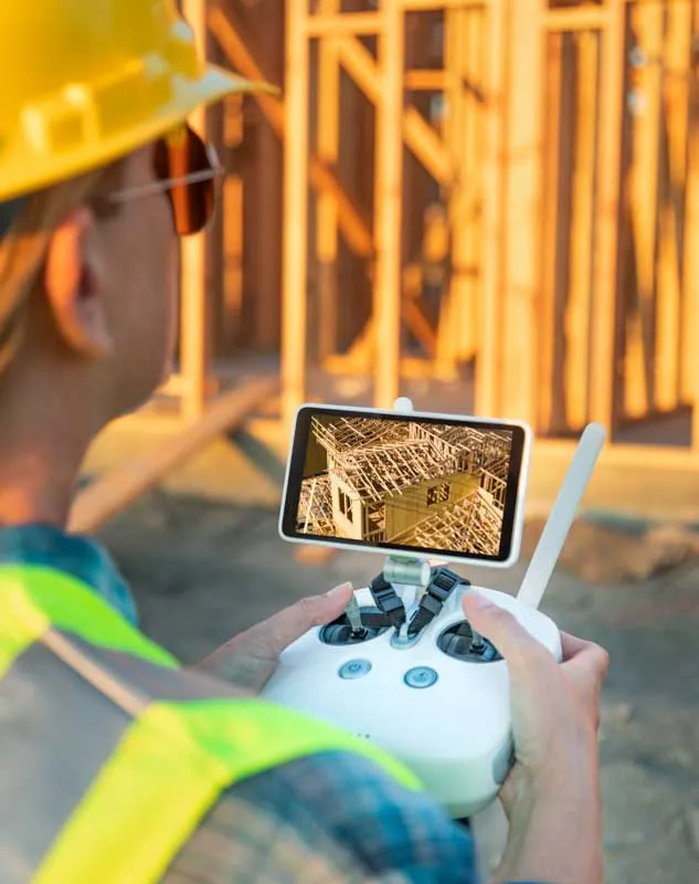 Man in a hard hat and high via jacket flying a filming a survey image of a construction project