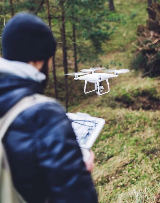 A man flying a DJI Phantom drone hovering above the ground in the woods
