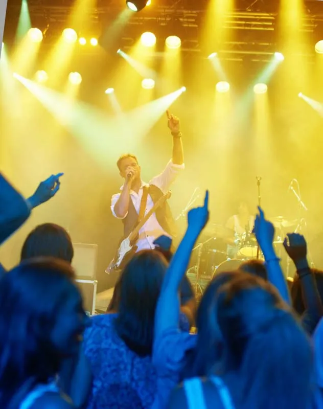 A musician on stage with yellow lights and a crowd of people in the foreground