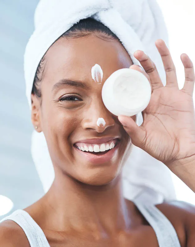 A dark skinned woman holding a beauty product to her eye