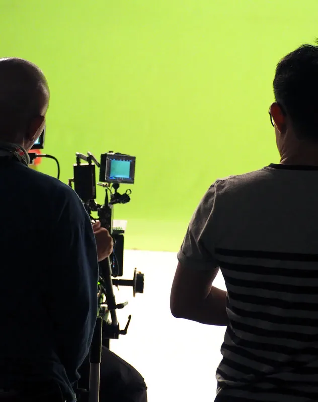 Silhouette of two camera people in a studio with a green screen background