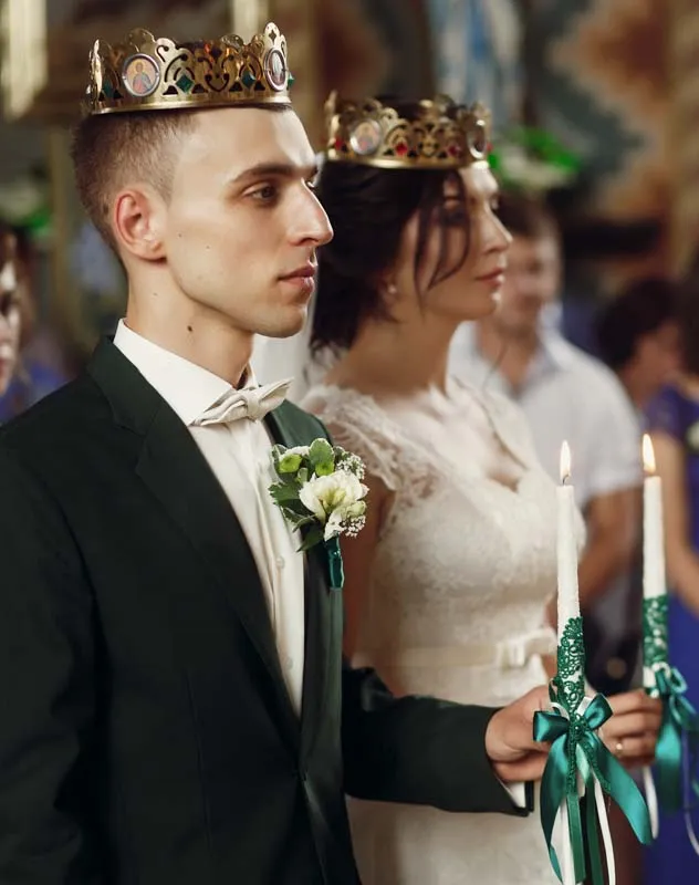 Couple wearing crowns and holding candles during a wedding ceremony