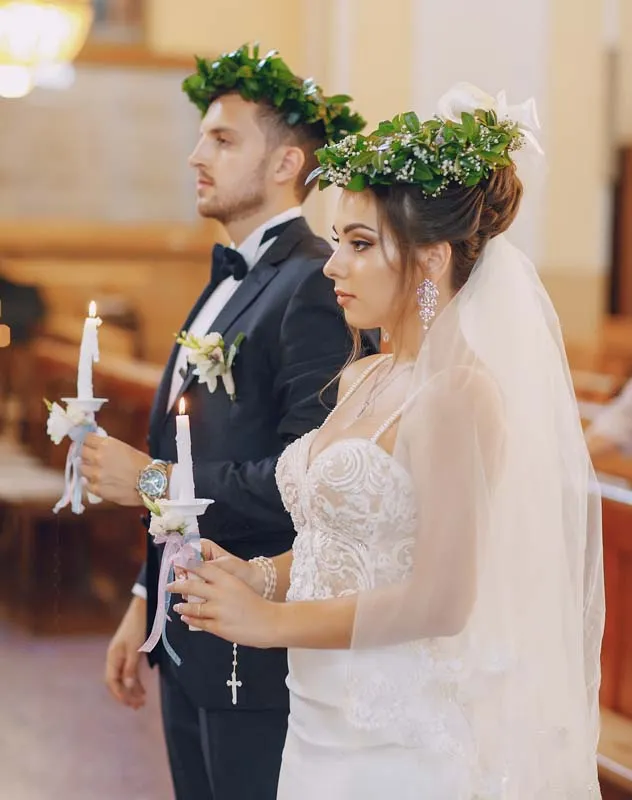 Couple wearing laurel leaf crowns and holding candles during a Orthodox wedding ceremony