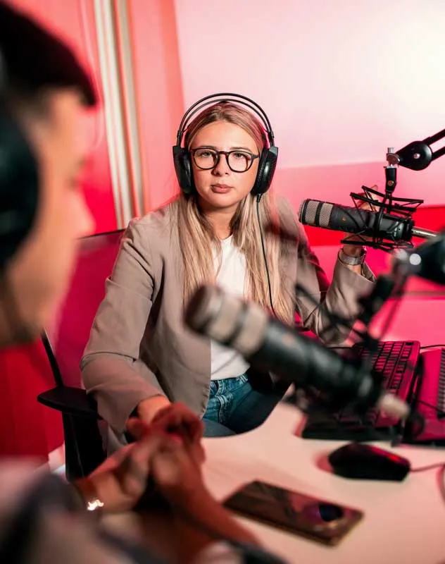 Two people wearing headphones chatting in a podcast recording studio