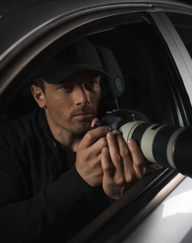 A man sat in a car taking photographs with a long lens