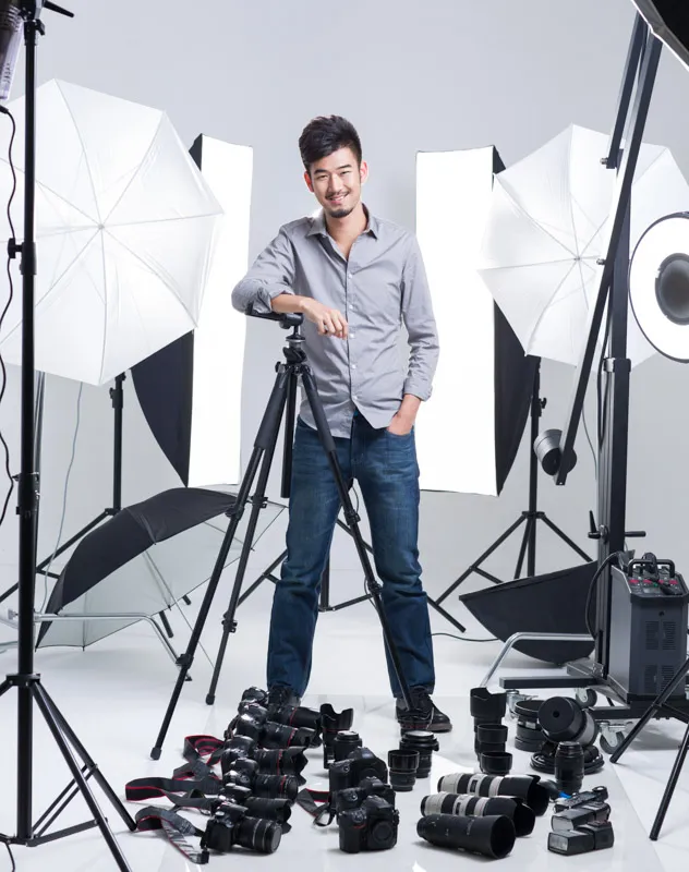 A studio manager standing with a ranging of cameras, lenses and lighting equipment