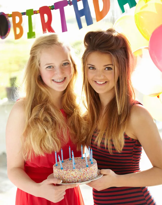 Two sixteen year old girls standing with a birthday cake
