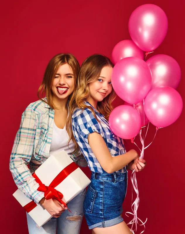 Two 16 year old girls standing together with present and balloons