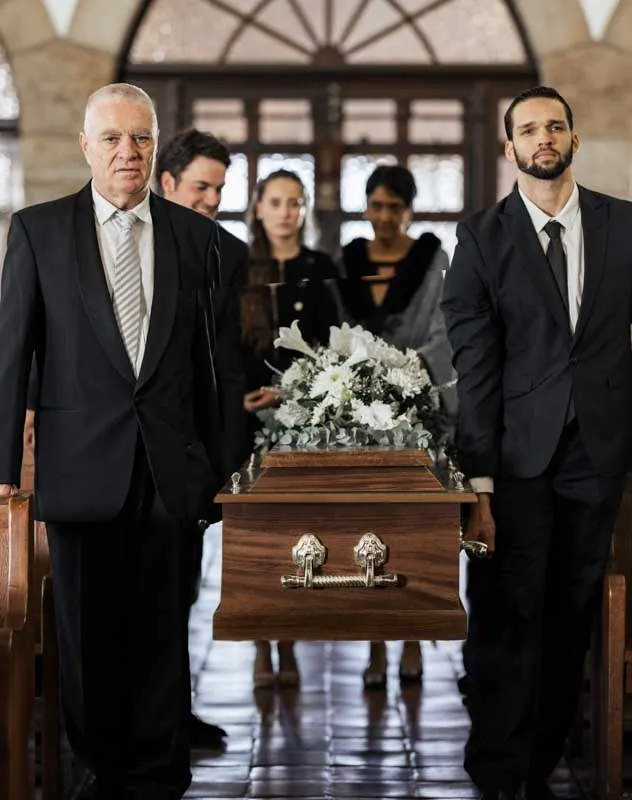 Pallbears standing next to a coffin with memorial flowers on top