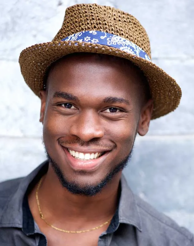 A head and shoulders shot of a good-looking man in a hat smiling whilst having his picture taken