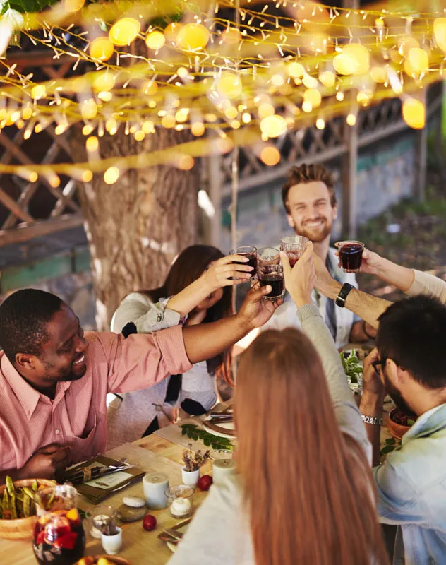 A group of people celebrating together with a toast over dinner underneath twinkling lights