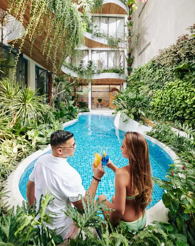 A promotional image of a couple sat next to a pool in a green indoor space