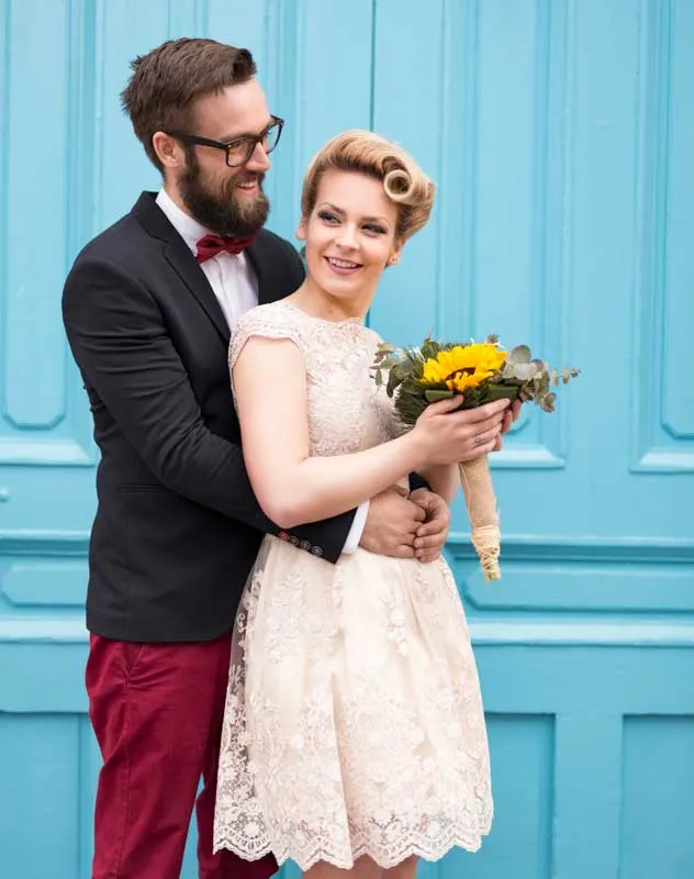 Groom standing next to a bride holding flowers in front of a blue door